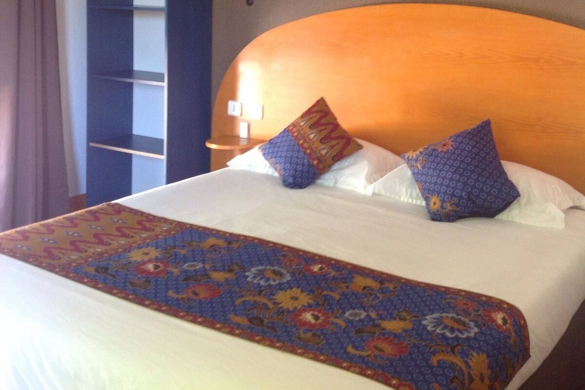 Una habitación de hotel con una cama grande, cabecero de madera y una lámpara de pared decorativa.