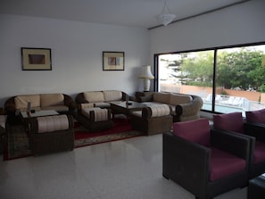 A living room with a sofa, armchairs, a coffee table, and a view of a swimming pool. - Hotel Kamal (Agadir)