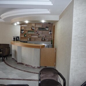 A bar area with a curved counter, shelves of bottles and glasses, and a coffee machine.