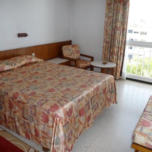 Una habitación de hotel con una cama grande, una silla, una mesita y una ventana con cortinas.