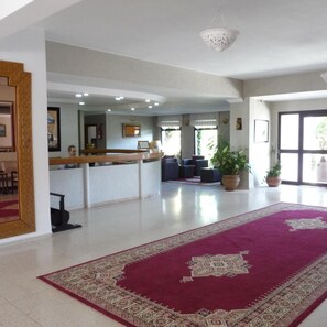 A spacious lobby with a reception desk, seating area, and potted plants.