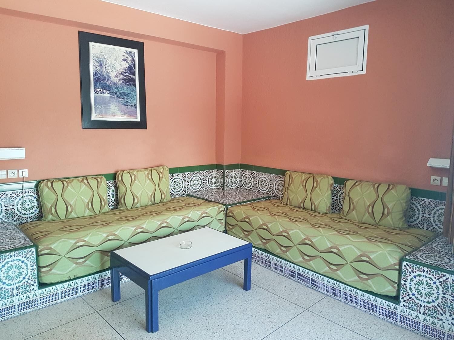 A living room with a sofa set, a coffee table, patterned tiles, and a framed picture on the wall.