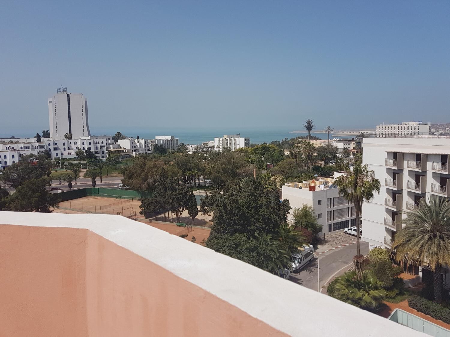 Un paysage urbain côtier avec des bâtiments modernes, un ciel dégagé et une vue sur la mer.