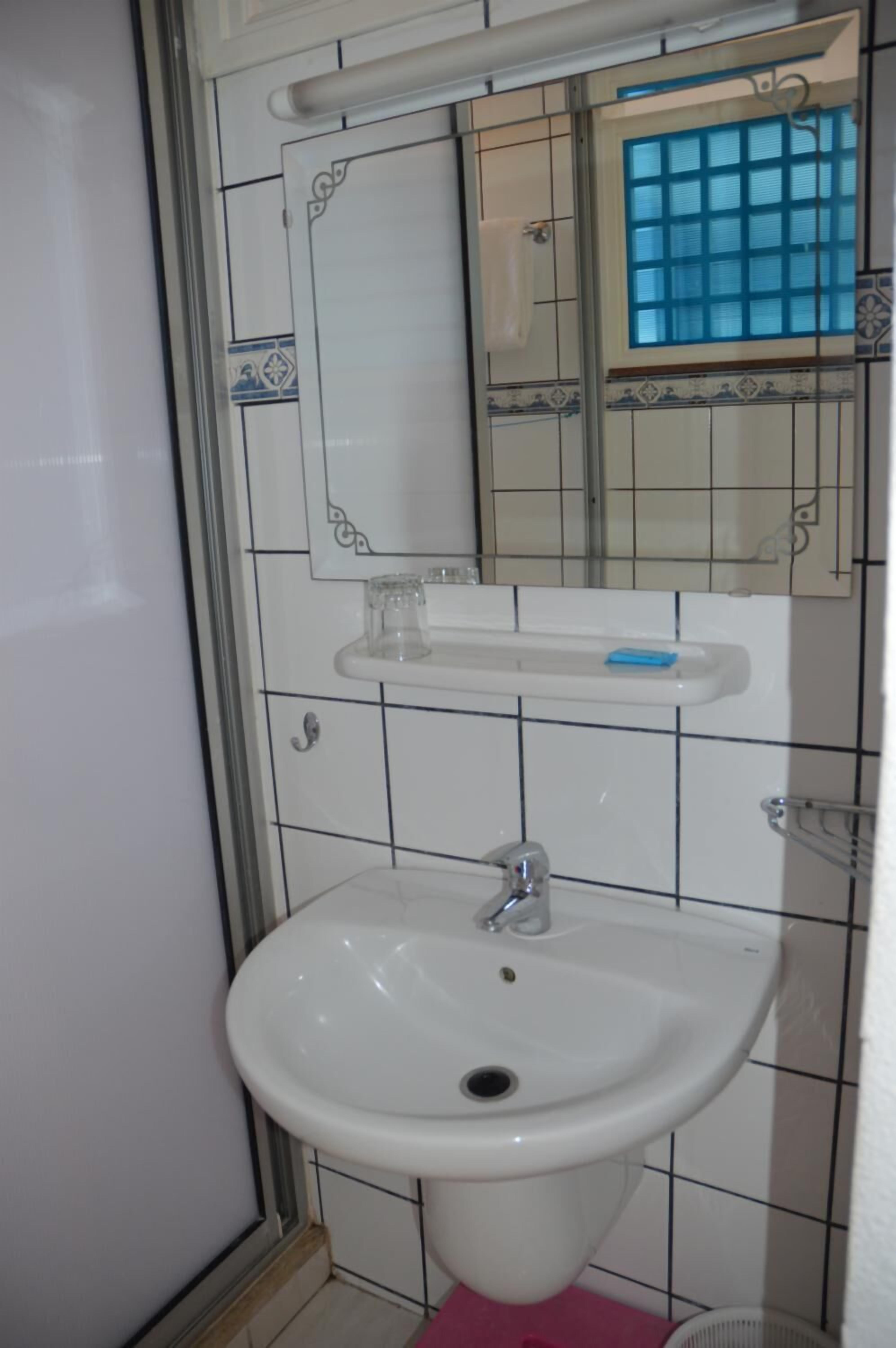 A bathroom with a white sink, a mirror, and a window with blue-tinted glass.