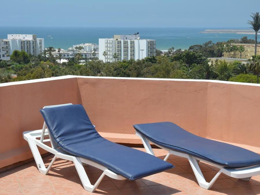 A balcony with two sun loungers and a view of the sea and buildings.