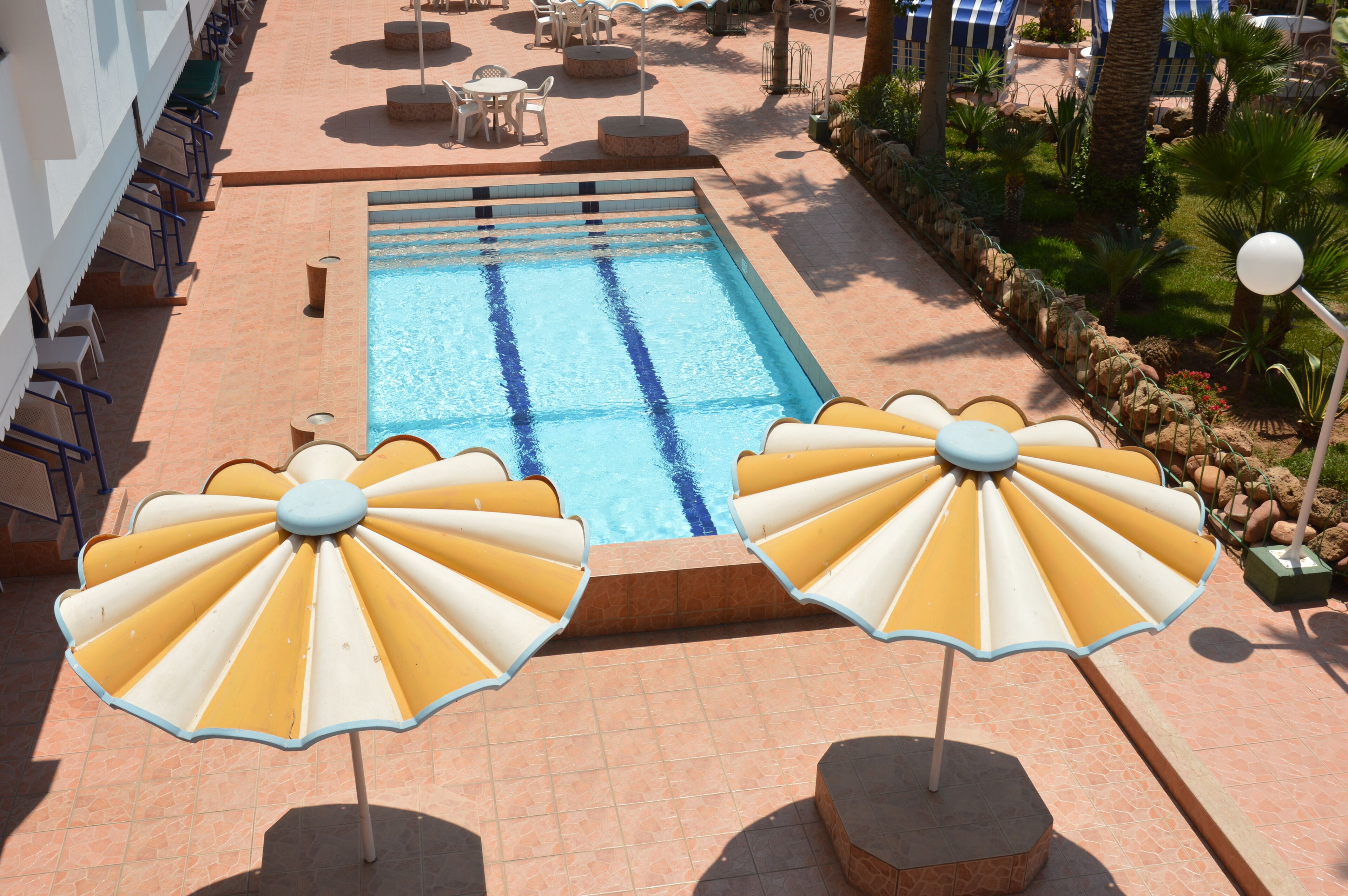A swimming pool with two sun umbrellas, lounge chairs, and a tiled patio area.