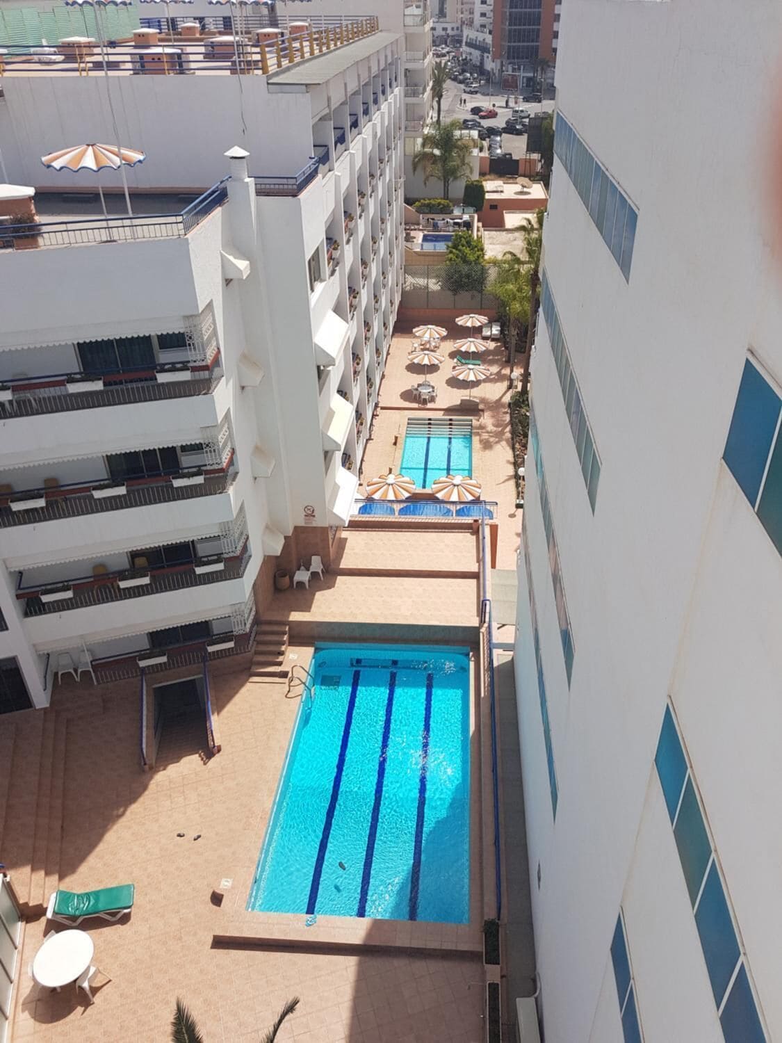 A multi-story hotel with a rooftop swimming pool, outdoor seating, and a view of the surrounding buildings.