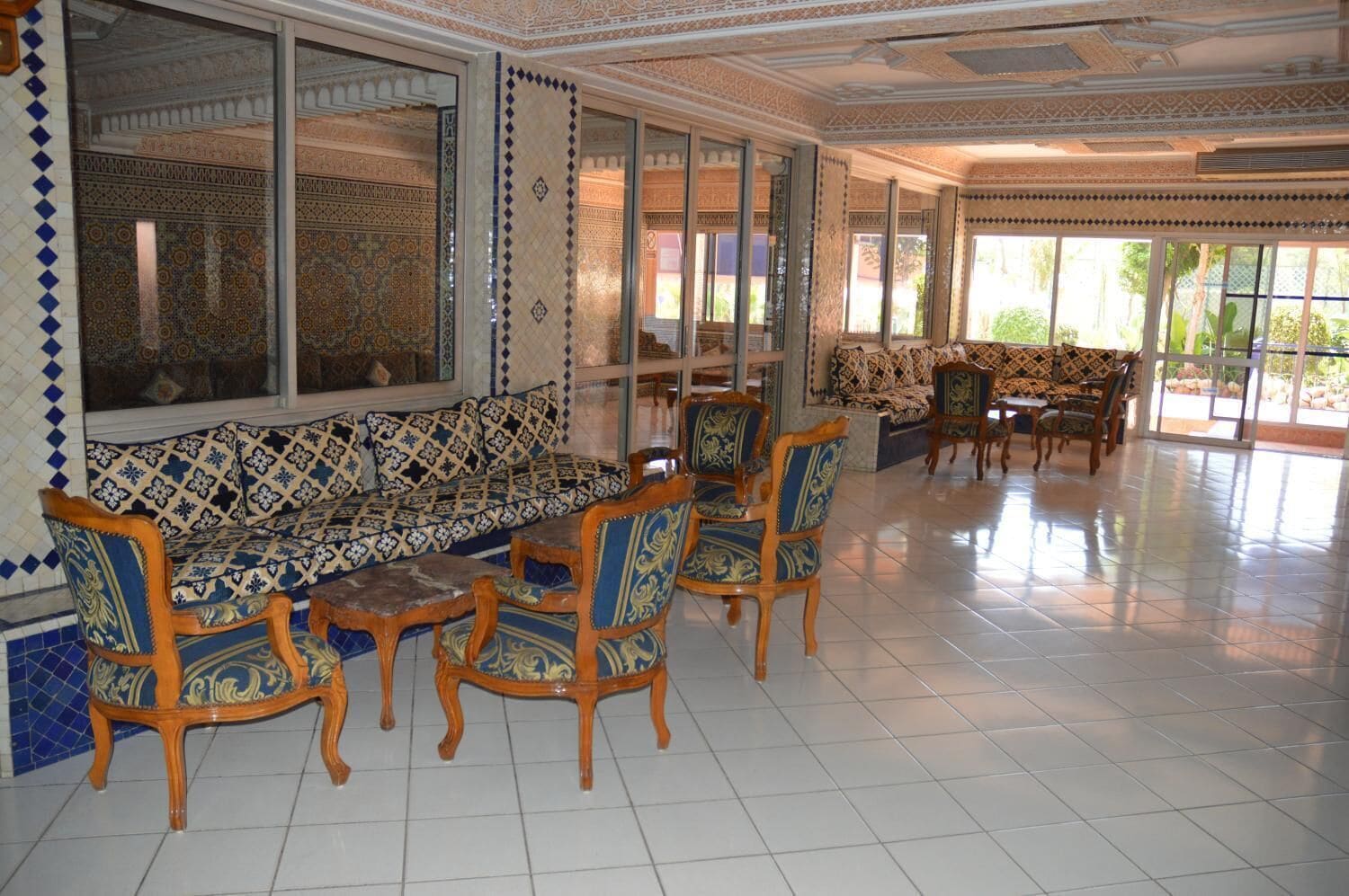 A spacious room with a patterned sofa set, wooden chairs, and a tiled floor.