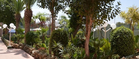 A landscaped garden with a variety of trees, a paved walkway, and a metal fence.