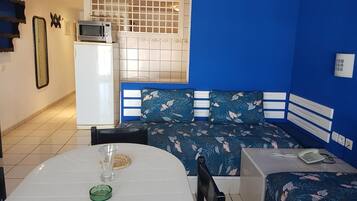 A compact room with a kitchenette, a dining area with a table and chairs, and a bed with a floral bedspread.