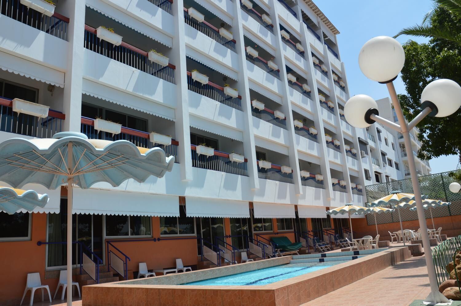A multi-story hotel with balconies, a swimming pool, and outdoor seating areas.