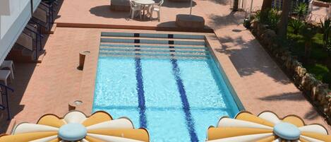 A swimming pool with sun umbrellas and lounge chairs, surrounded by a tiled patio area.