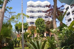 A multi-story building with balconies, surrounded by lush greenery and palm trees.