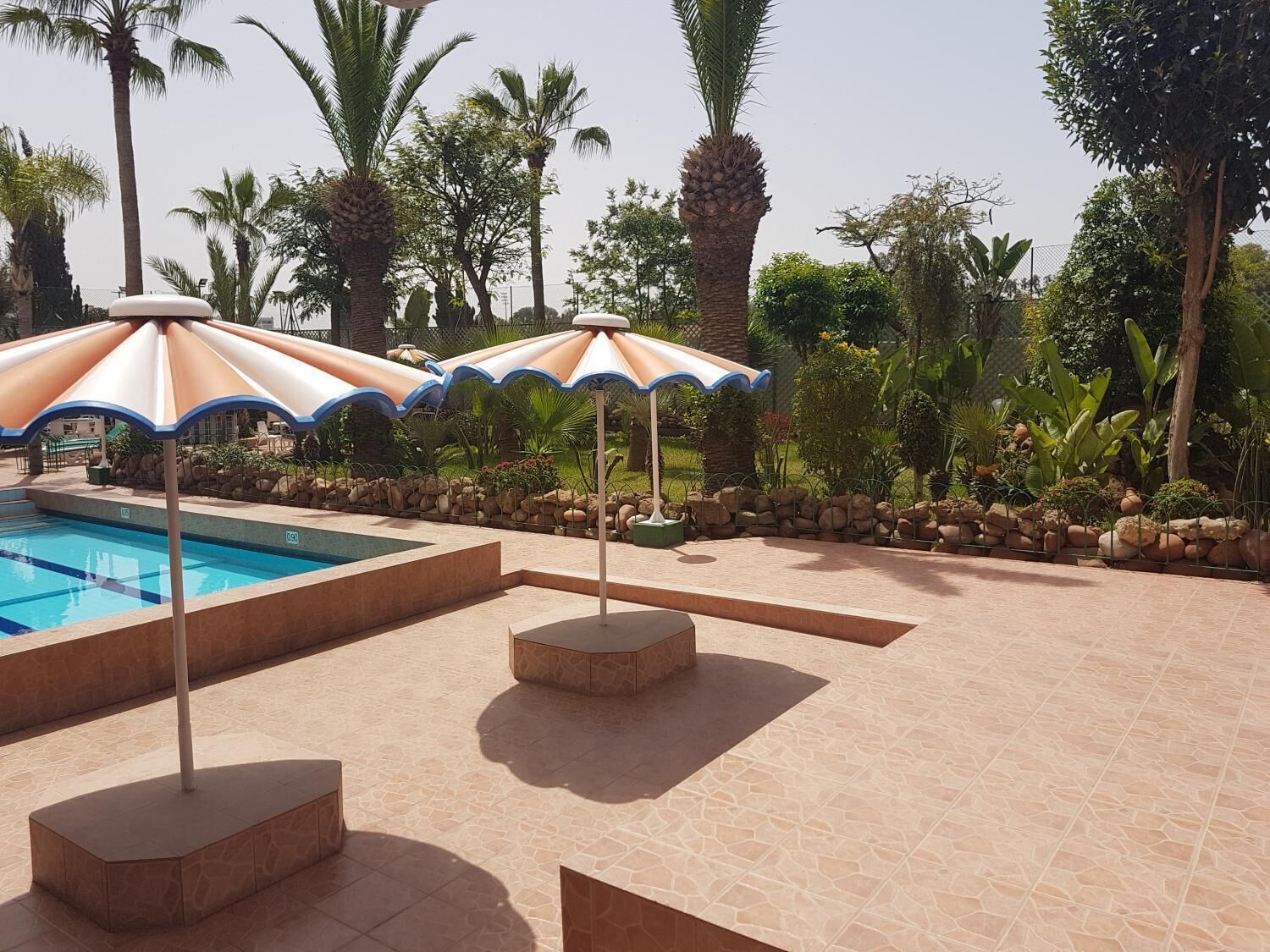 A swimming pool with three umbrellas and a stone-tiled deck.