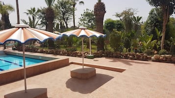 A swimming pool with three umbrellas and a stone-tiled deck.