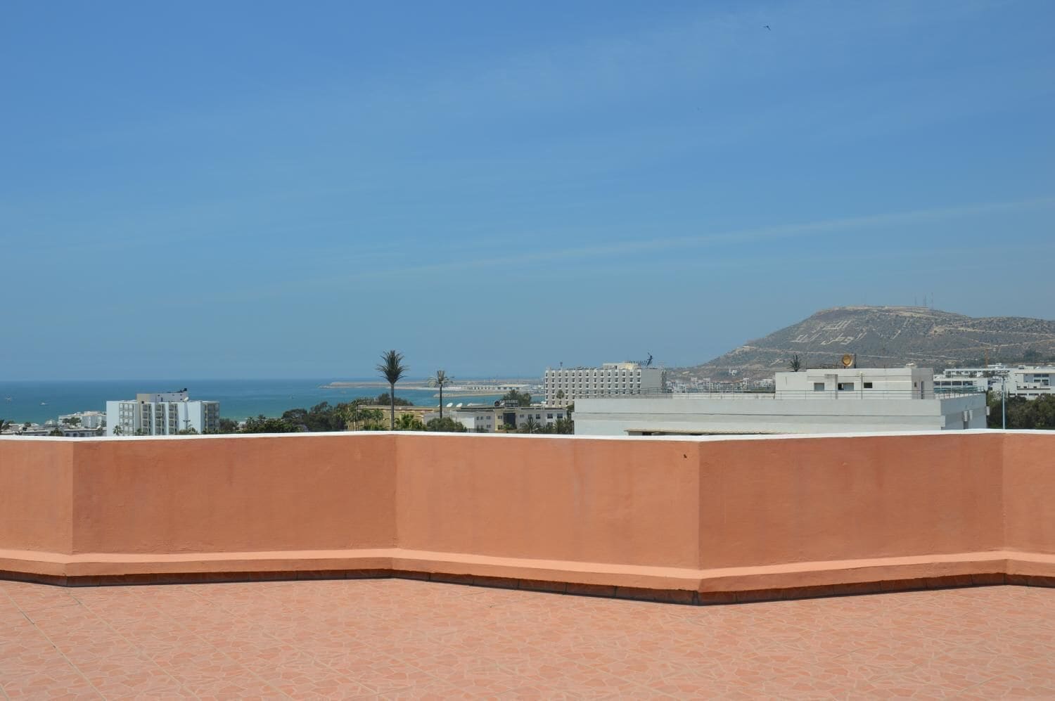 A rooftop terrace with a view of the sea and buildings in the background.