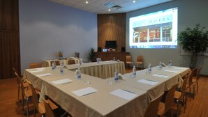 A conference room with a long table, chairs, water bottles, and a projector screen displaying a hotel image. - Suite Hotel Merlot (Majzoub)