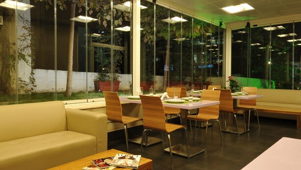 A restaurant with glass walls, wooden furniture, and a view of the outdoors. - Suite Hotel Merlot (Majzoub)