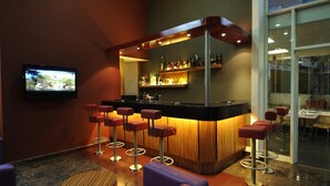 A bar area with a counter, stools, and a television screen. - Suite Hotel Merlot (Majzoub)