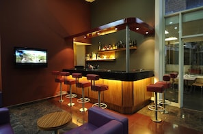 A bar area with a counter, stools, and a television screen. - Suite Hotel Merlot (Majzoub)