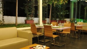 A restaurant with a modern interior, featuring wooden tables and chairs, a sofa, and a magazine on a table. - Suite Hotel Merlot (Majzoub)