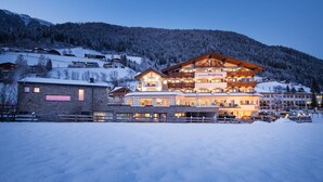 Un hotel de varios pisos con un telesilla visible al fondo, rodeado de montañas cubiertas de nieve.