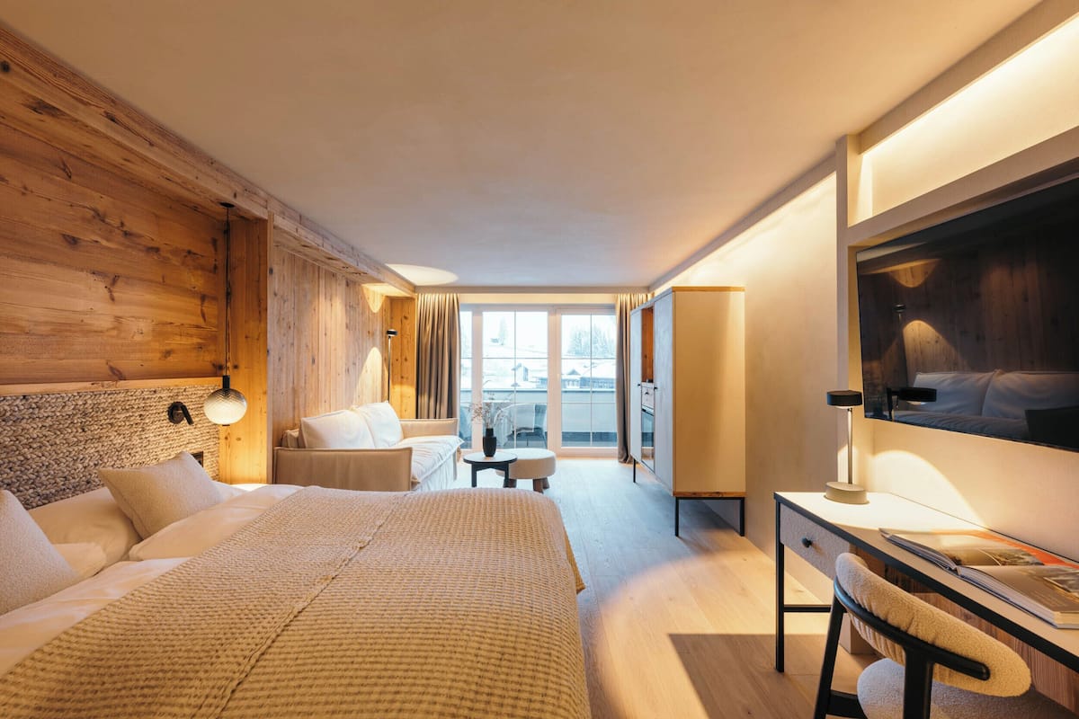 Habitación de hotel con una cama grande, un escritorio, una silla, una mesita y un ventanal con vistas a la ciudad.