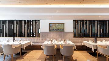 Un restaurante con varias mesas preparadas para comer, una zona de estar con banco acolchado y un cuadro grande en la pared.