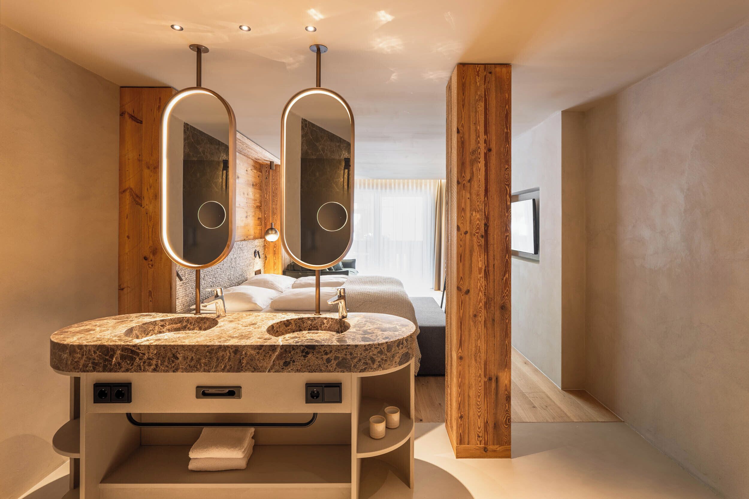 A modern bathroom with a marble sink, two mirrors, wooden accents, and a built-in towel rack.
