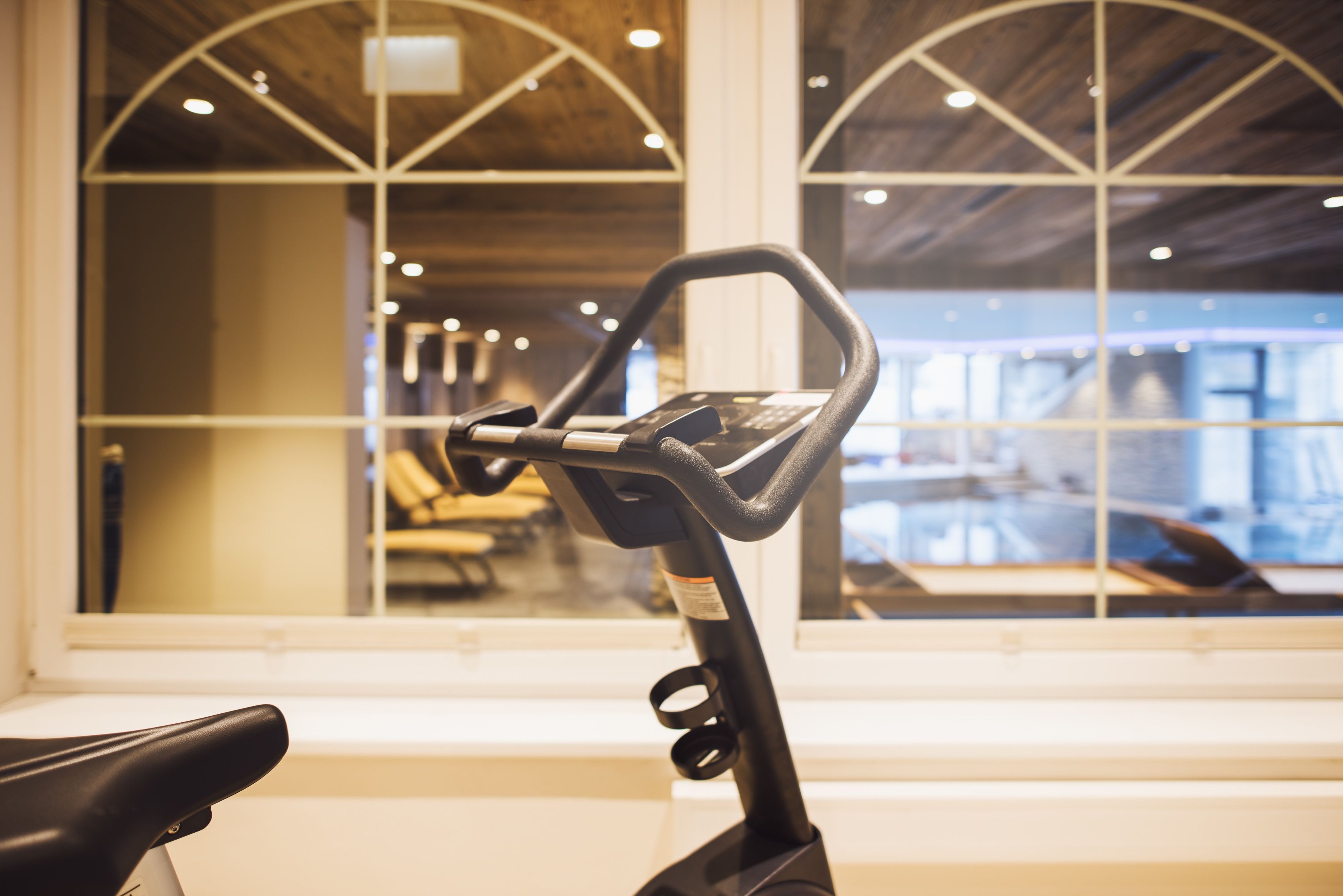 A stationary bike in a room with large windows and a view of a car outside.