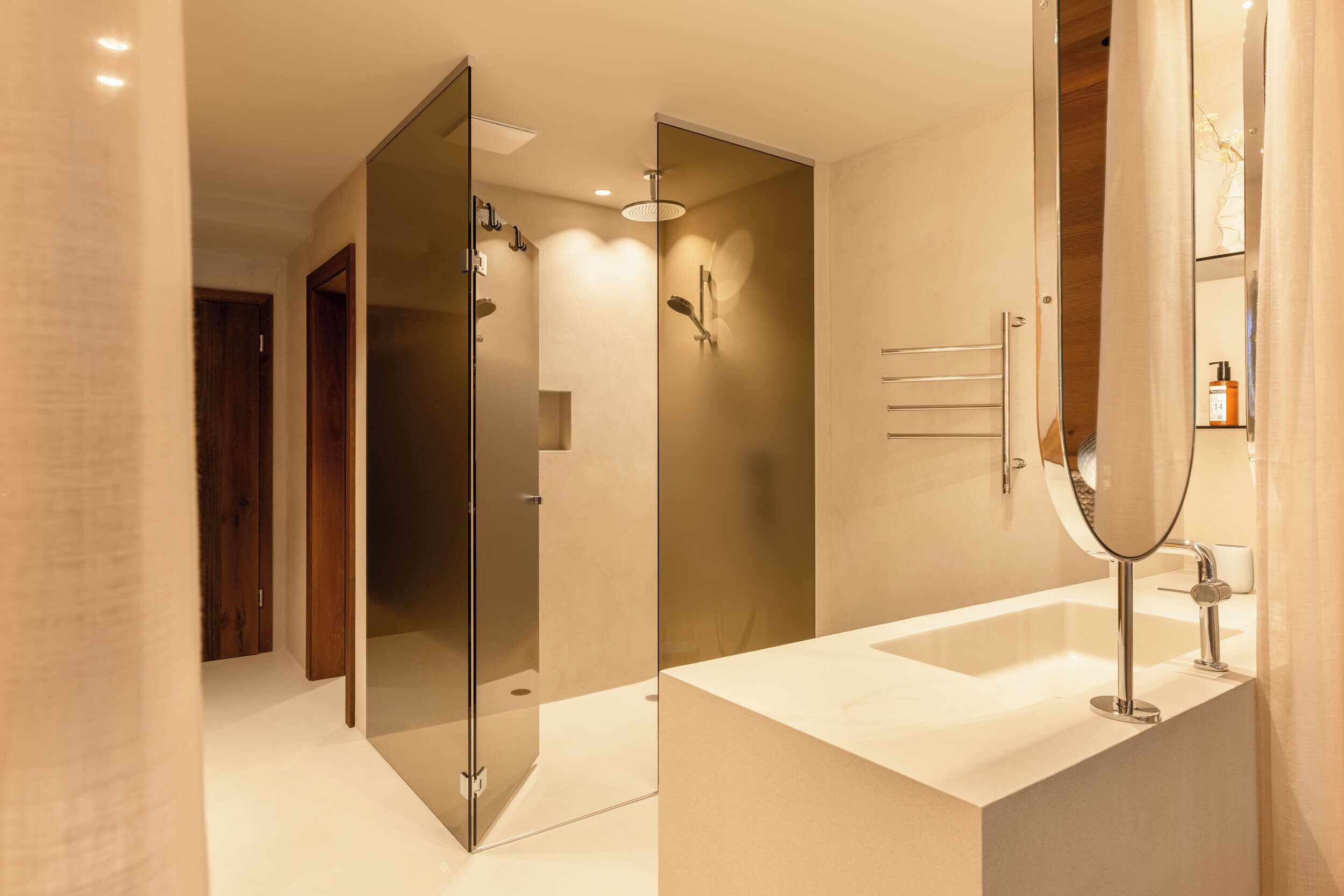 A modern bathroom with a glass shower enclosure, a large mirror, and a white sink.