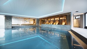 Una piscina interior moderna con superficie de agua cristalina, paredes de piedra y paneles de madera.
