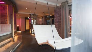 A modern hotel lobby with a hanging chair, a reception desk, and a staircase.