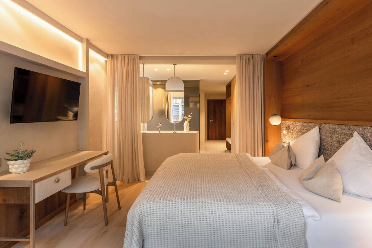 Una habitación de hotel moderna con cama, escritorio, silla, televisión y baño visible a través de una puerta abierta.