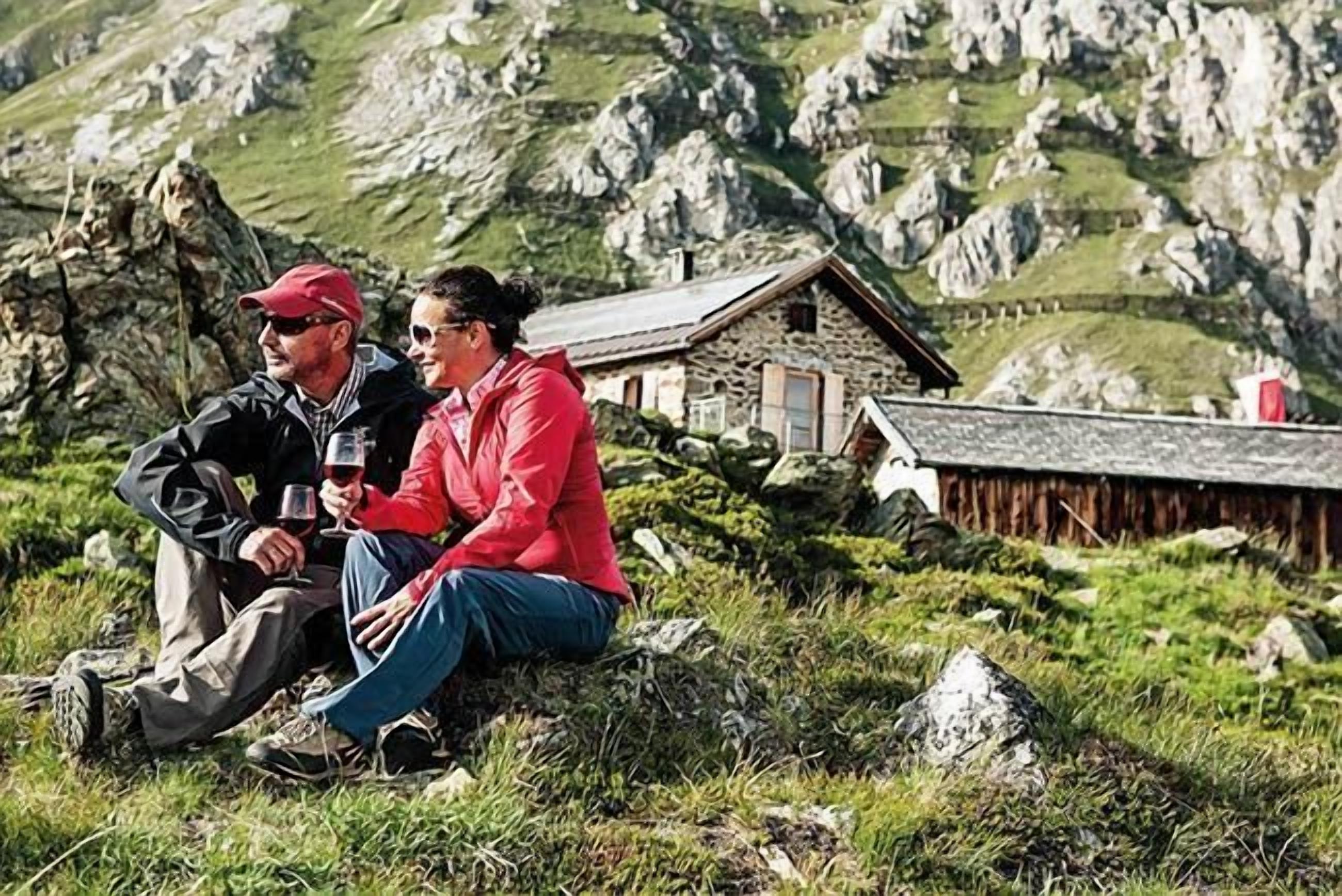 Two people sitting on a grassy area with a stone building in the background.