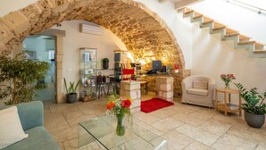 A living room with a stone archway, a staircase, a sofa, a coffee table with flowers, and a red rug. - Boutique Hotel Fortino (Chania)