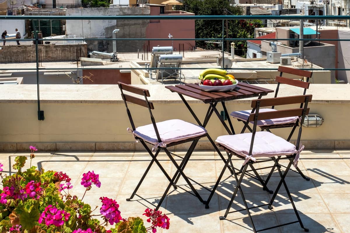 A rooftop terrace with a table and chairs, overlooking a cityscape with buildings and a mosque.