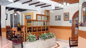 A lobby with a reception desk, a wooden bookshelf, and a planter with green plants. - Hotel Ambalá Bogotá Colonial (Bogotá)