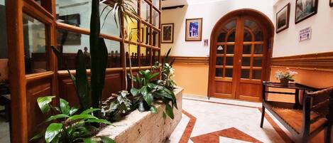 Un vestíbulo con piso de mármol, bancos de madera, una exhibición de plantas y un amplio arco de entrada.