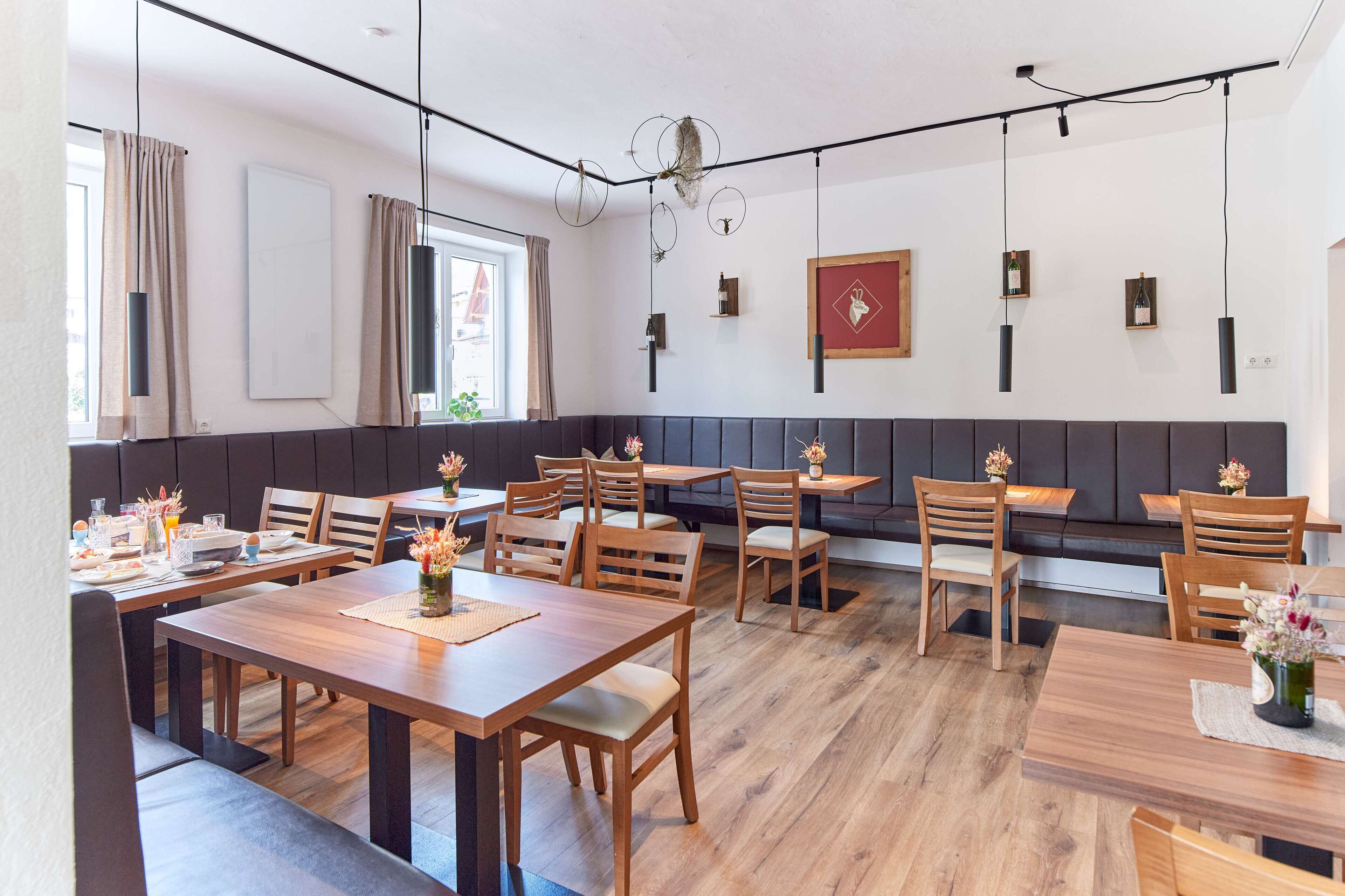 Un comedor moderno con mesas y sillas de madera, una zona de estar con banco, e iluminación colgante.