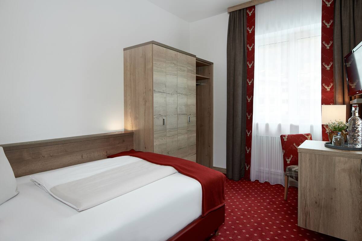 Een hotelkamer met een bed, een houten garderobe, een bureau met een lamp en een televisie.