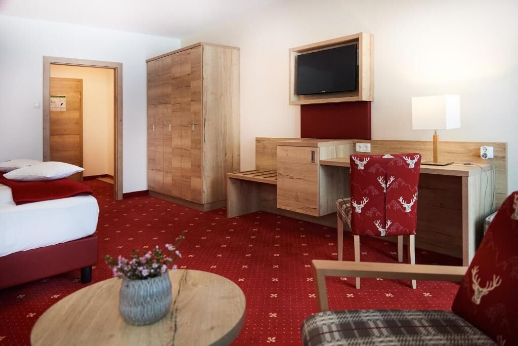 Quarto de hotel com uma cama, uma escrivaninha, uma cadeira, uma televisão e um abajur.