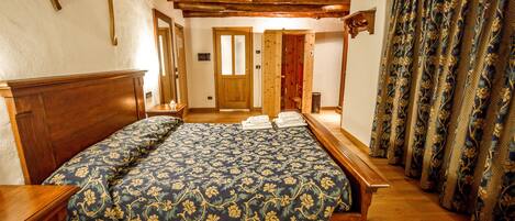 Un dormitorio con cama de madera, una mesita de noche de madera, un televisor montado en la pared y una cortina estampada.