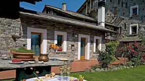 Un edificio de piedra con una terraza acondicionada para comer, que incluye una mesa con platos de comida y bebidas.