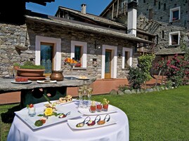 Un edificio de piedra con una terraza acondicionada para comer, que incluye una mesa con platos de comida y bebidas.