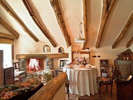 Un interior rústico con vigas de madera a la vista, una chimenea, una mesa redonda lista para una comida y un rincón de estar acogedor.