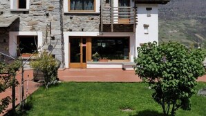 Un edificio de piedra con un balcón de madera, puerta de entrada de vidrio y vistas a montañas.