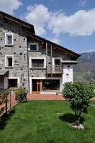 Un edificio de piedra con un balcón de madera, puerta de entrada de vidrio y vistas a montañas.