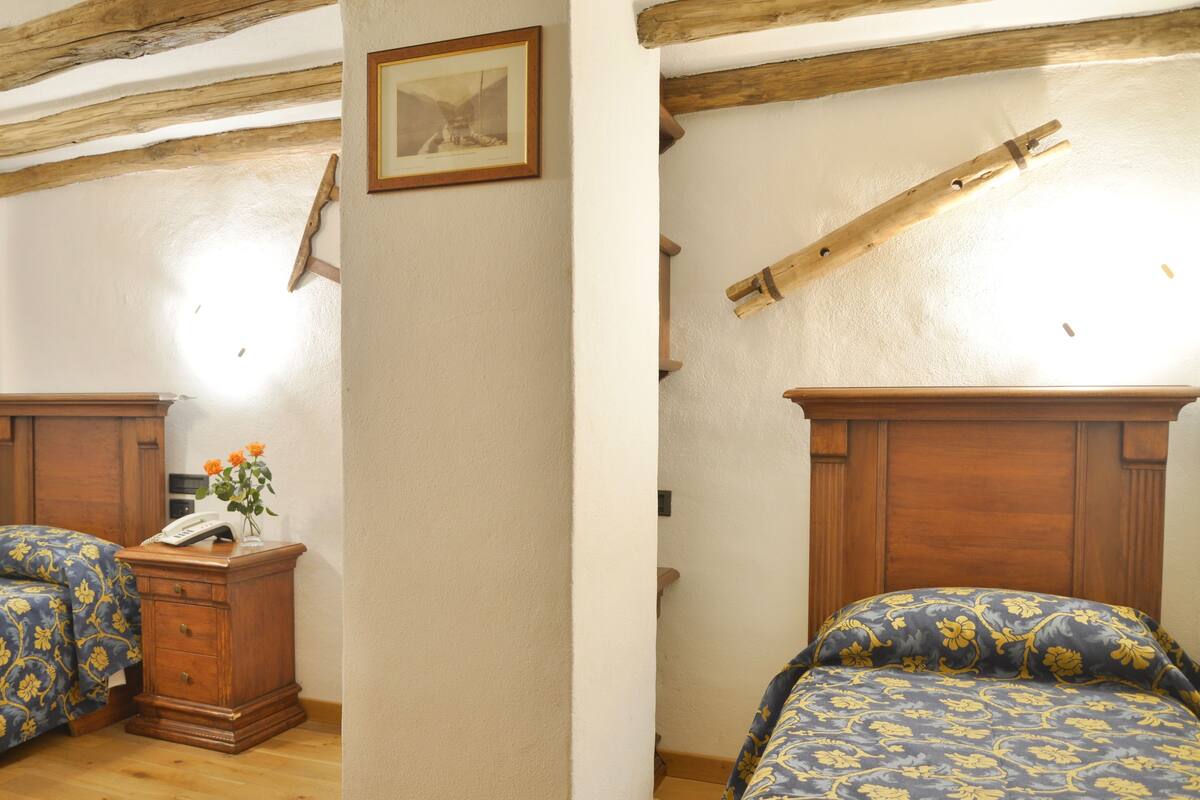Une chambre avec deux lits, des têtes de lit en bois, une table de chevet avec un téléphone et un tableau encadré au mur.