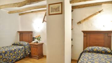 A bedroom with two beds, wooden headboards, a nightstand with a telephone, and a framed picture on the wall.